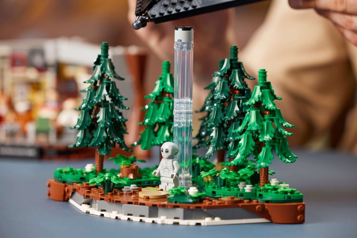 LEGO Ideas X-Files set 21369 featuring white alien minifigure among evergreen trees and glass structure.