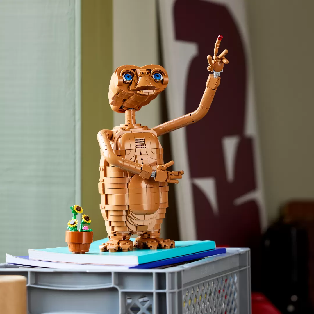 LEGO E.T. figure with glowing heart on books and crate, with small potted flowers nearby.