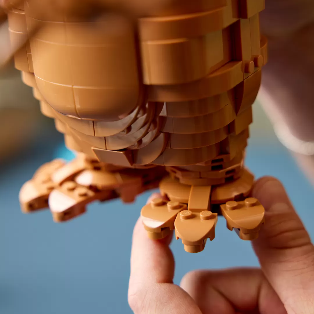 LEGO E.T. figure with glowing heart piece held in child's hand against blue background.