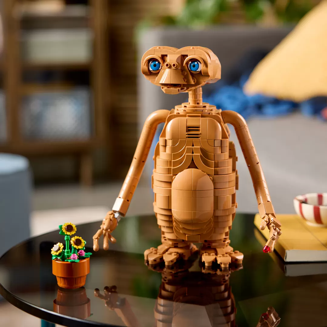 LEGO E.T. buildable figure with glowing blue eyes and illuminated chest, displayed on black table with potted flowers.