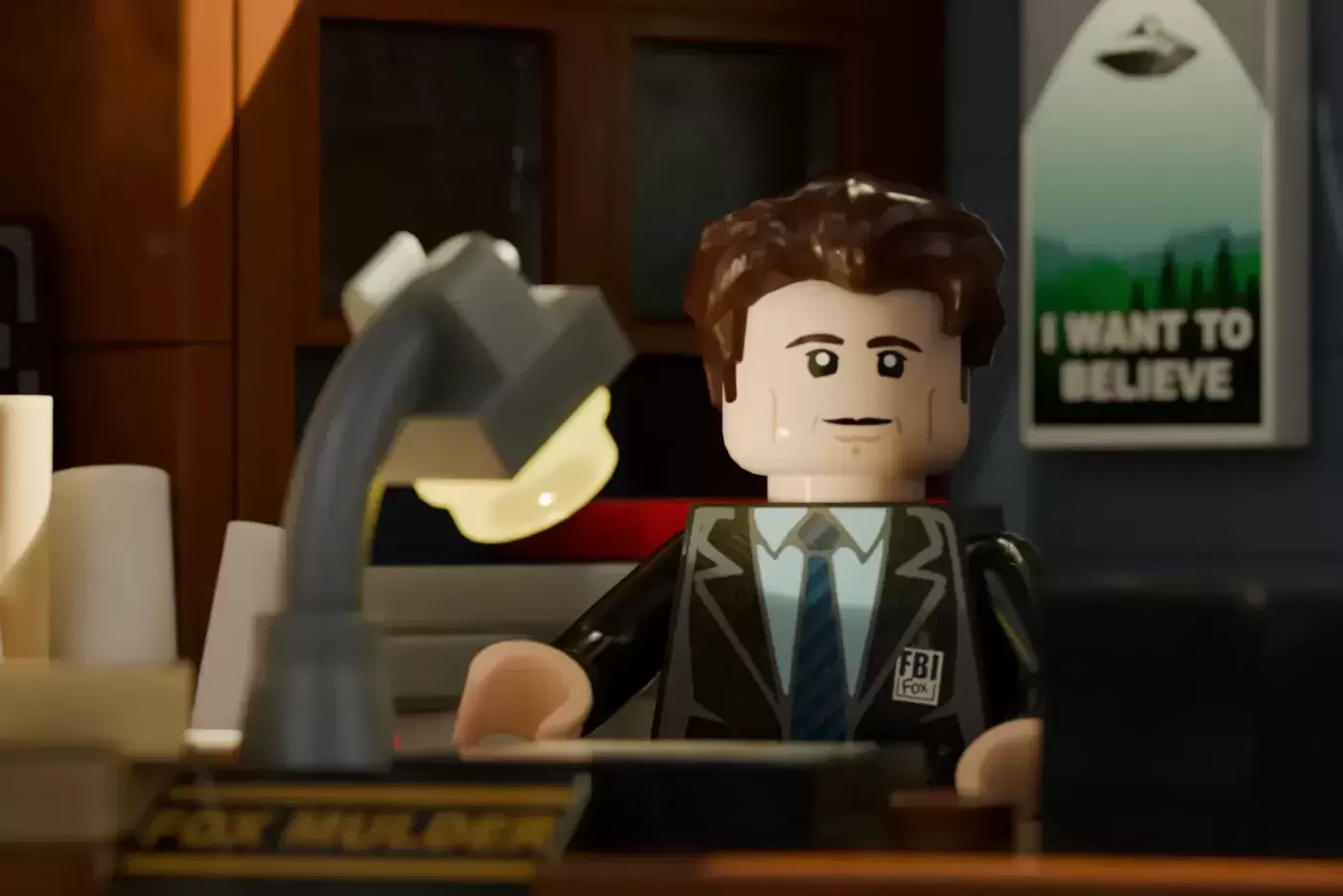 LEGO minifigure FBI agent at desk in X-Files office set with UFO poster and desk lamp visible.