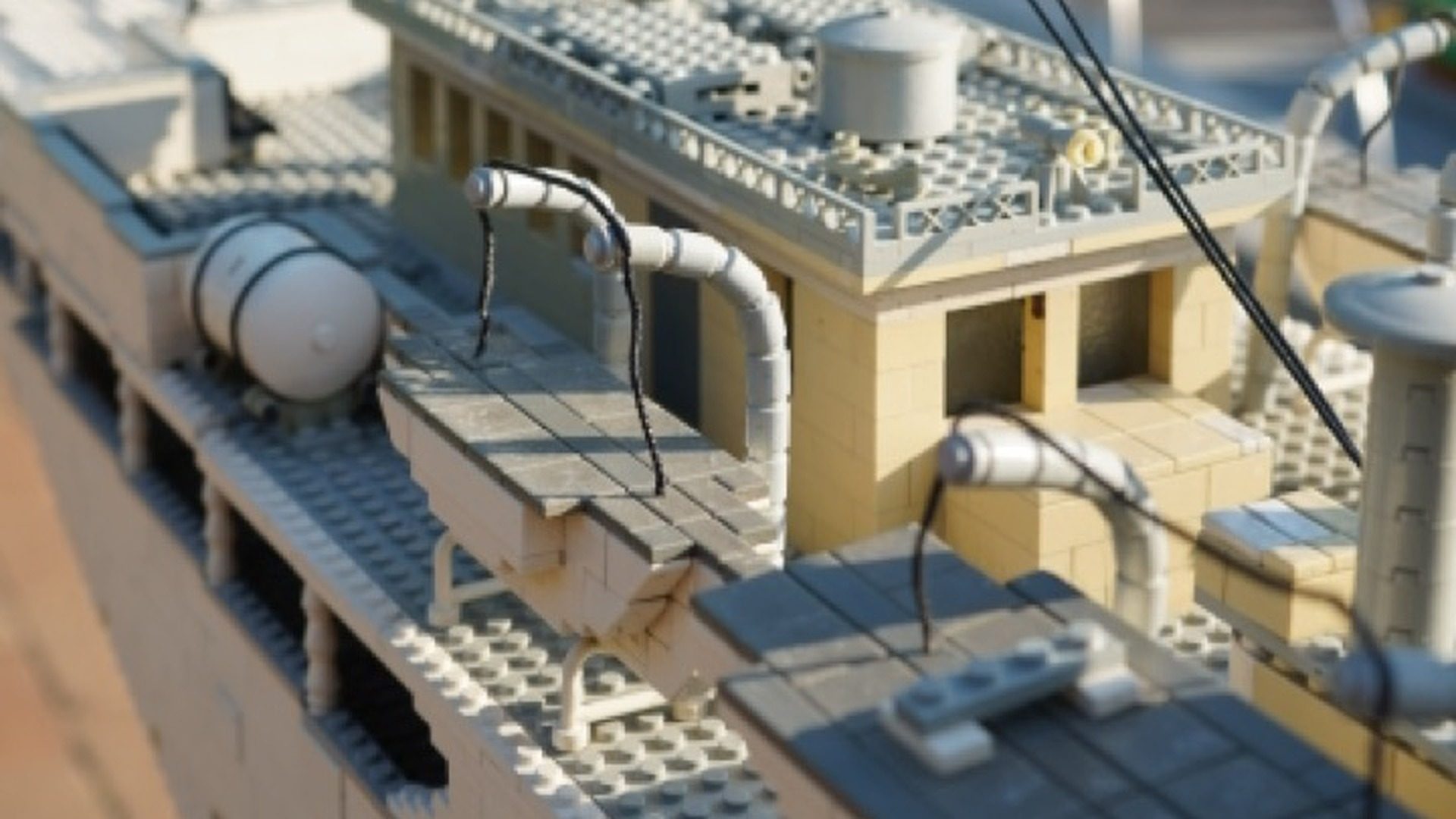 LEGO rooftop scene with miniature buildings, chimneys, and detailed architectural elements in cream and blue colors.