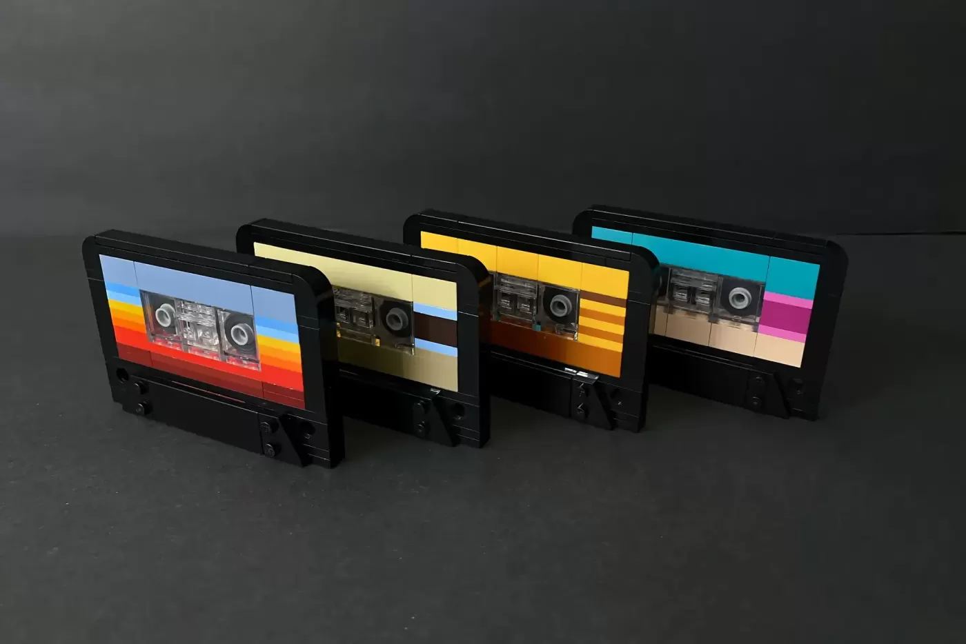 Four LEGO boomboxes with colorful tape designs displayed in a row on gray surface.
